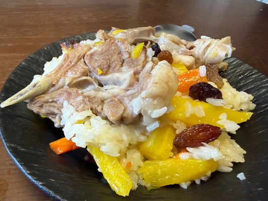 A plate of homemade Lamb Pilaf with tender lamb, yellow carrots, and dried fruit on a dark wooden table